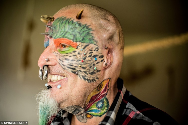 Ted Richards, 56, from Hartcliffe in Bristol, who has had his ears taken off so he can look more like his Parrot. August 16 2015. See SWNS story SWPARROT; A man who had his face and eyeballs tattooed to look like his pet parrots has gone a step further - by cutting off his EARS. Bonkers Ted Richards, 56, is obsessed by pets Ellie, Teaka, Timneh, Jake and Bubi and has his face tattooed with colourful feathers. But the animal nut - who has 110 tattoos, 50 piercings and a split tongue - has now had both his ears removed by a surgeon in a six hour operation. Eccentric Ted has given his severed ears to a friend who "will appreciate them" and is now planning to find a surgeon prepared to turn his nose into a BEAK.
